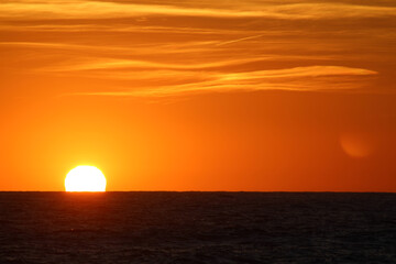 Sun on horizon. Tranquil scenery of sunset on sea. Calm sea water, cloudy orange sky. Beautiful evening on the beach. 