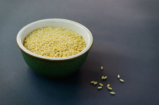 Raw risoni pasta in a green bowl against a dark background. The concept of proper nutrition. Risoni is suitable for making salads. Horizontal orientation.