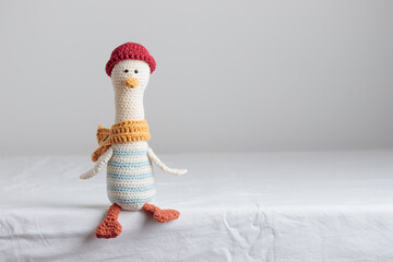Cute handmade crochet knitted amigurumi toy goose, sailor in red hat and yellow scarf, sits on the white table, handicraft crocheted banner with copy space