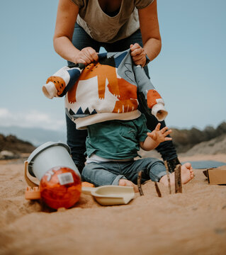 Escena familiar de una madre desvistiendo a su beb&eacute; en la playa rodeado con sus juguetes.