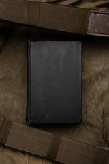 A closed book with a black cover on an old hiking backpack. Vintage khaki canvas back.