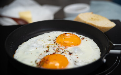 Close up of fried eggs with spices and seasonings in hot frying pan. Breakfast