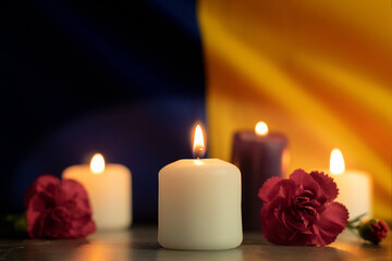 A group of burning candles and flowers on the background of the national flag of Ukraine