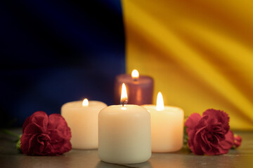Fototapeta na wymiar A group of burning candles and flowers on the background of the national flag of Ukraine