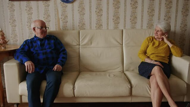 Senior Relationship Problems Concept. Two Elderly European Retired Pensioner Couple Sitting On A Leather Beige Couch Far Apart In A Cosy Old-fashioned Apartment . High Quality 4k Footage