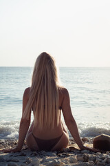 Fototapeta na wymiar Young woman with long hair sitting on the beach. Summer holiday concept, peace and relaxation.