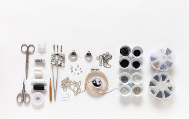 Flat lay of process of embroidering a broach in form of black and white symbol of yin and yang with beads, bugle, rhinestones and gimp. Tools and sets of beads on white background. Fashion hobby