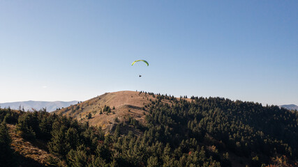Paraglider flying in the blue sky with mountain in background.