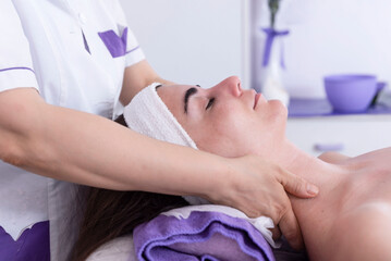 Fototapeta na wymiar Esthetician performing professional facial massage on woman's face in spa clinic. Anti-aging massage with face lift. Professional lymphatic drainage massage in the beauty salon