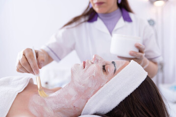 Obraz na płótnie Canvas Cosmetologist applying a face mask to a client's face in a beauty salon, spa