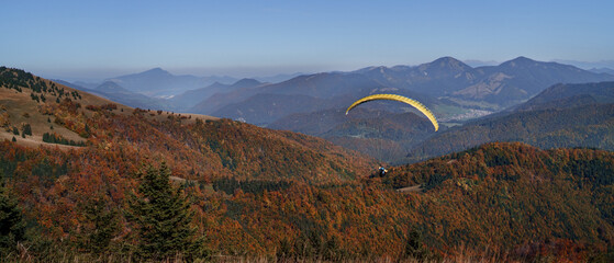 Paraglider flying in the blue sky with mountain in background.