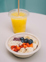 Un plato de frutas cortadas tipo acai bowl acompañado de un zumo natural