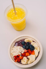 Un plato de frutas cortadas tipo acai bowl acompañado de un zumo natural