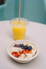 Un plato de frutas cortadas tipo acai bowl acompañado de un zumo natural