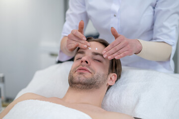 Obraz na płótnie Canvas Young man having face massage in a spa salon