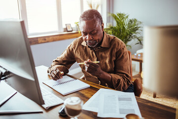 Senior man working at PC computer at home. African American man calculating finances. Shot of a...