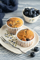 Muffins with blueberry and lavender in rustic style. Cupcakes on the ceramic plate with a pattern of blueberries. Bowl full of blueberry, small fork. Mini cakes on the grey wooden table