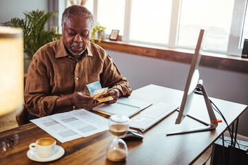 Cropped shot of a senior man sitting alone in his living room and reading his financial budgets. Serious mature man wearing glasses sitting on couch in living room manage budget