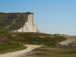 Sunlit white chalk cliffs under summery blue skies near Seaford, with a path snaking off to the distance and inviting one to explore.