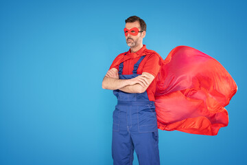 Handsome handyman in red cape and mask as a super hero isolated on blue studio background . Repair home concept.