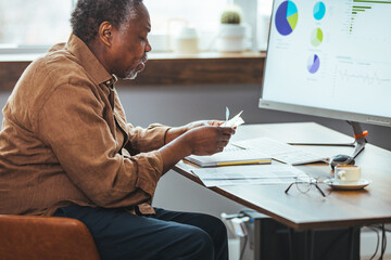 Stressed elderly grey-haired man in glasses look at laptop screen have problems paying bills taxes online. Thoughtful mature 70s male manage household finances, calculate expenses expenditures at home