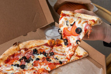The girl holds a piece of pizza in her hand. Fast food, unhealthy food, food delivery.