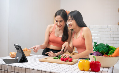 Beautiful homosexual Lesbian couples learning to cooking healthy meals, stay healthy in shape.Asian woman LGBTQ+,LGBT,LGBTQ 
 home online kitchen.Wellness lifestyle.Tablet learning.Salad Diet foods .