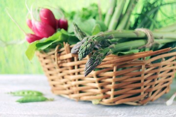 Obraz premium Asparagus, radishes and green onions in a wicker basket, on a wooden table, against the backdrop of a lawn, harvest season, organic natural food, healthy food, home cooking 