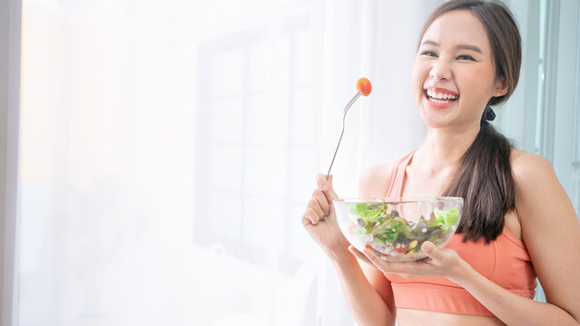Portrait of Asian attractive woman hold salad bowl. Beautiful sport girl in sportswear enjoy eat clean vegetables after exercise for health in house.Diet and Healthy food concept.Banner cover design.