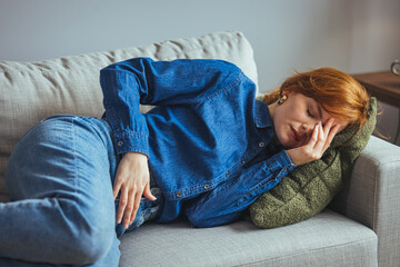 Young sick woman with hands holding pressing her crotch lower abdomen. Medical or gynecological problems, healthcare concept. Young woman suffering from abdominal pain while laying on sofa at home