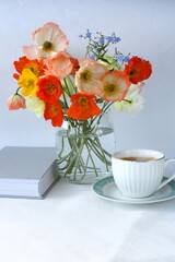 A cup of coffee, a book and a bouquet of field poppies. Vertical photo.