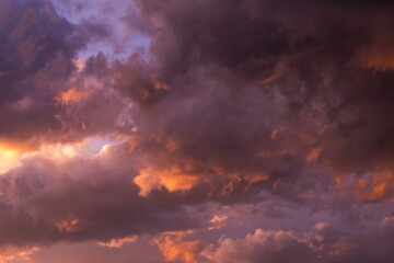 Epic sunset storm sky. Big grey violet cumulus thunderstorm clouds in orange sunlight background texture
