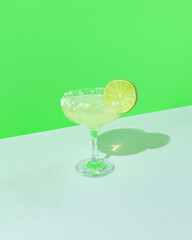 Minimal  composition with cocktail glass and fresh sliced lime against geometric green background. Tropical refreshment idea with copy space.