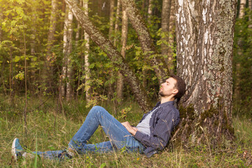 Young man alone lying, resting and relaxing in summer forest on green grass in sunlight. Rest and...