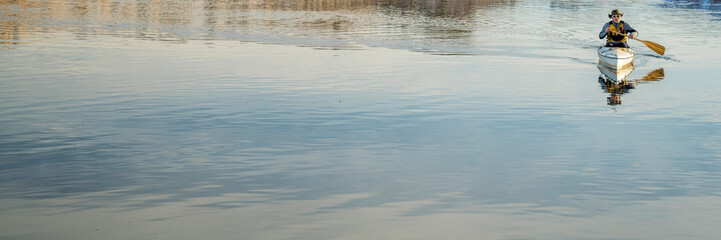 senior male wearing life jacket is paddling expedition canoe in winter scenery of Horsetooth Reservoir in northern Colorado, wide web banner
