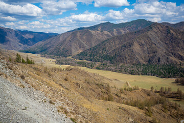 Scenic view from mountain pass to forest valley among mountain ranges and hills on horizon at changeable weather in spring time in Altai, Russia