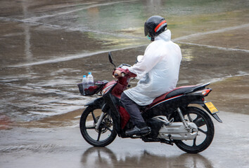 A man with a raincoat rides a motorcycle in the rain