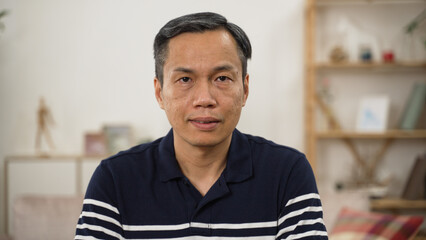 half length portrait of a grey haired Asian male pensioner in casual wear looking at camera with...