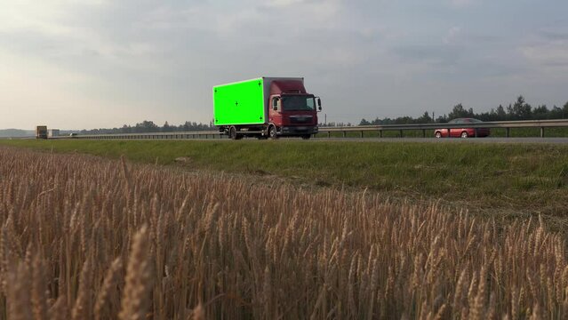 Cargo van with green screen and trackink markers on trailer drives along the highway past a wheat field. Mockup for adding your logo, slogan or company. Tansportation, courier service, delivery.