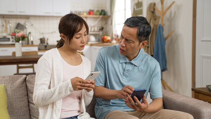 asian adult daughter helping senior dad with problem while they are using smartphones together in...