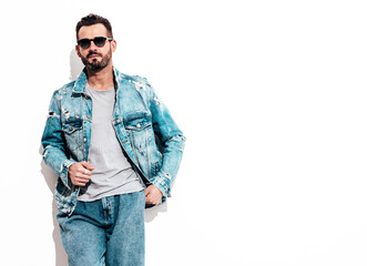 Fototapeta premium Portrait of handsome confident stylish hipster lambersexual model. Sexy man dressed in jeans jacket. Fashion male isolated on white wall in studio. In sunglasses