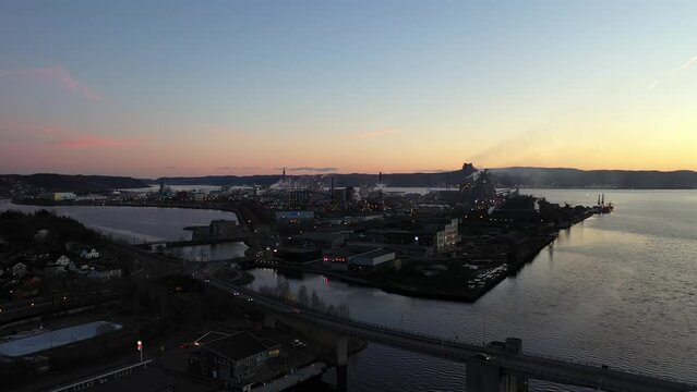 Silhouette with smoke from industrial island Heroya in Porsgrunn operated by Yara and Hydro - Late evening ascending aerial with sunset clouds in background - Norway