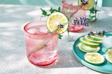 Cool lavender lemonade with lime slices and lavender flower on the table near pastel light blue background. Healthy organic summer soda drink. Detox water. Diet unalcolic coctail.