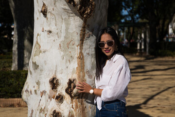 Very happy teenage girl hugging a huge tree trunk in the park with her eyes closed and a toothless...