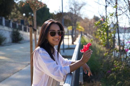 young and beautiful woman from south america touring europe. The woman is holding a red flower in her hands and is leaning on the railing by the river in seville. Travel and tourism concept.