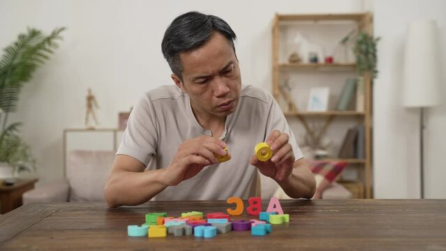 asian senior male Alzheimer&rsquo;s patient practicing rehab treatment with color letter bricks at home. he compares two blocks and puts them in order on table