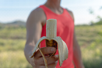 Athlete man showing a banana that is bitten. Frontal image of a young athlete who is holding an...