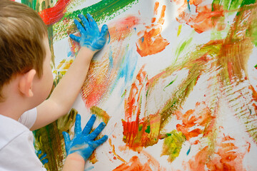 a child draws with paints on the wall, blue children's hands in paint. A fun activity for a child. photo of a grizontal.