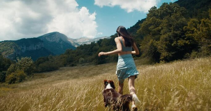 Excited carefree young adult woman run with bordercollie dog on mountain meadow. Inspired happy girl hike with domestic animal on summer vacation. Female traveler on lifestyle journey wanderlust