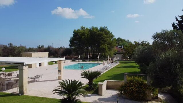 IT, Borgagne, 6.10.2021, Pool with blue water. Visitors wave their hand. Resting place on a hot day. A man teaches a child to swim. Drone. 